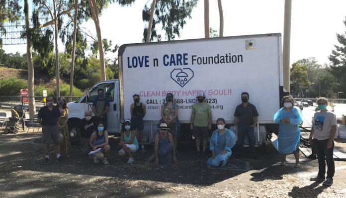 Volunteers stand in front of the Love N Care Foundation shower truck at an unhoused shower event on Figueroa Street in Los Angeles, CA.
